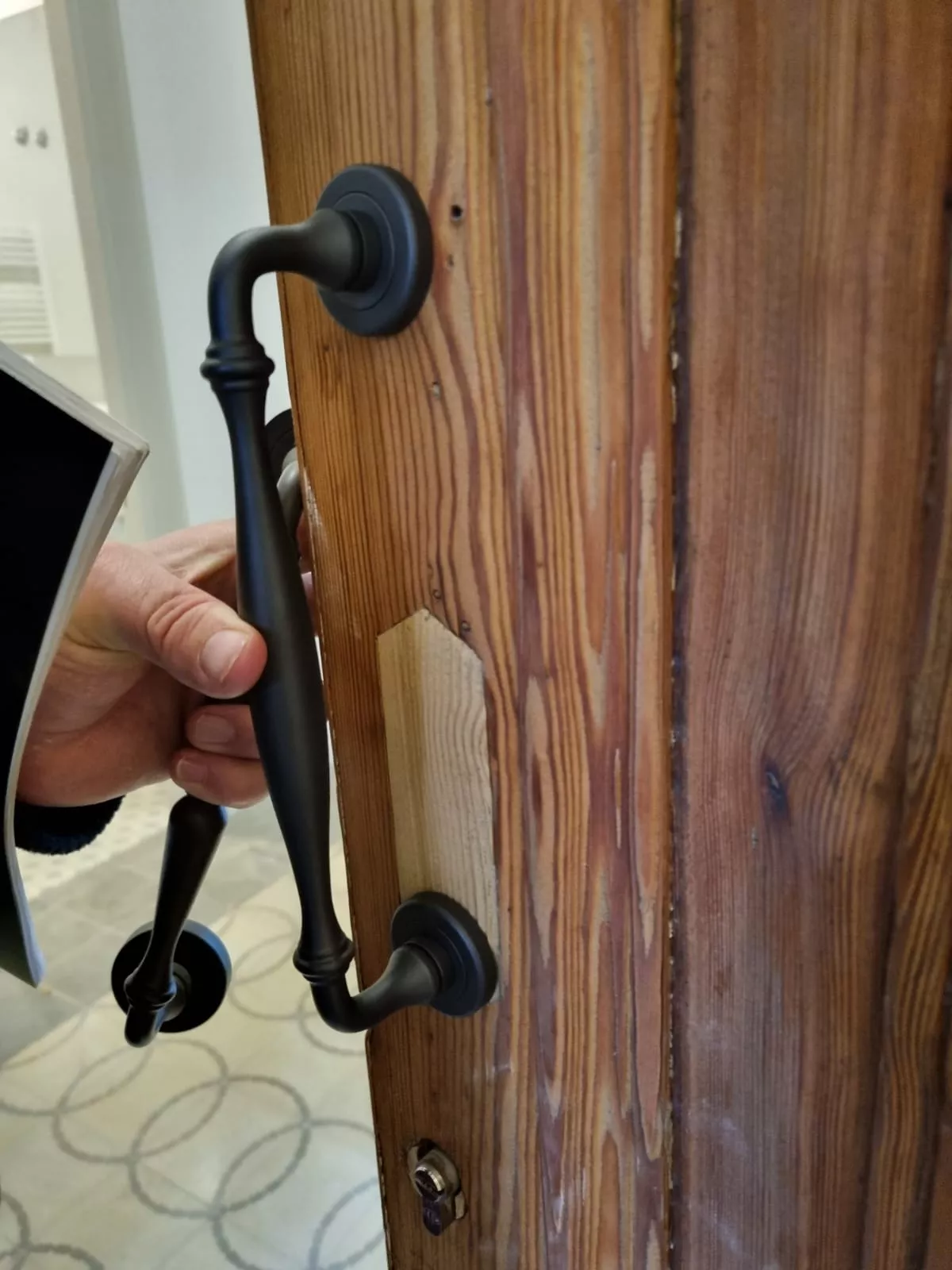 Detalle de mano abriendo puerta de madera rústica con manija de hierro forjado negro, proyecto CASA AAE.
