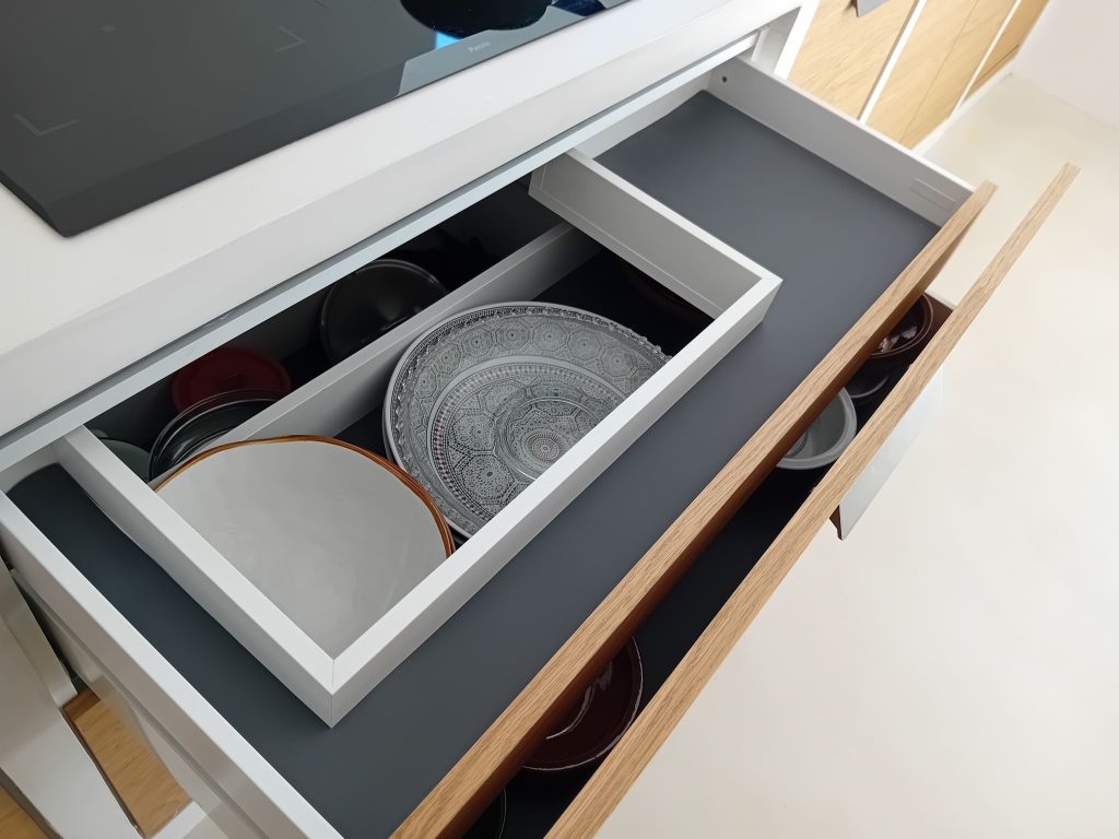 Cajón de cocina abierto con organizadores de madera y platos, mostrando el método de trabajo de la madera con precisión.