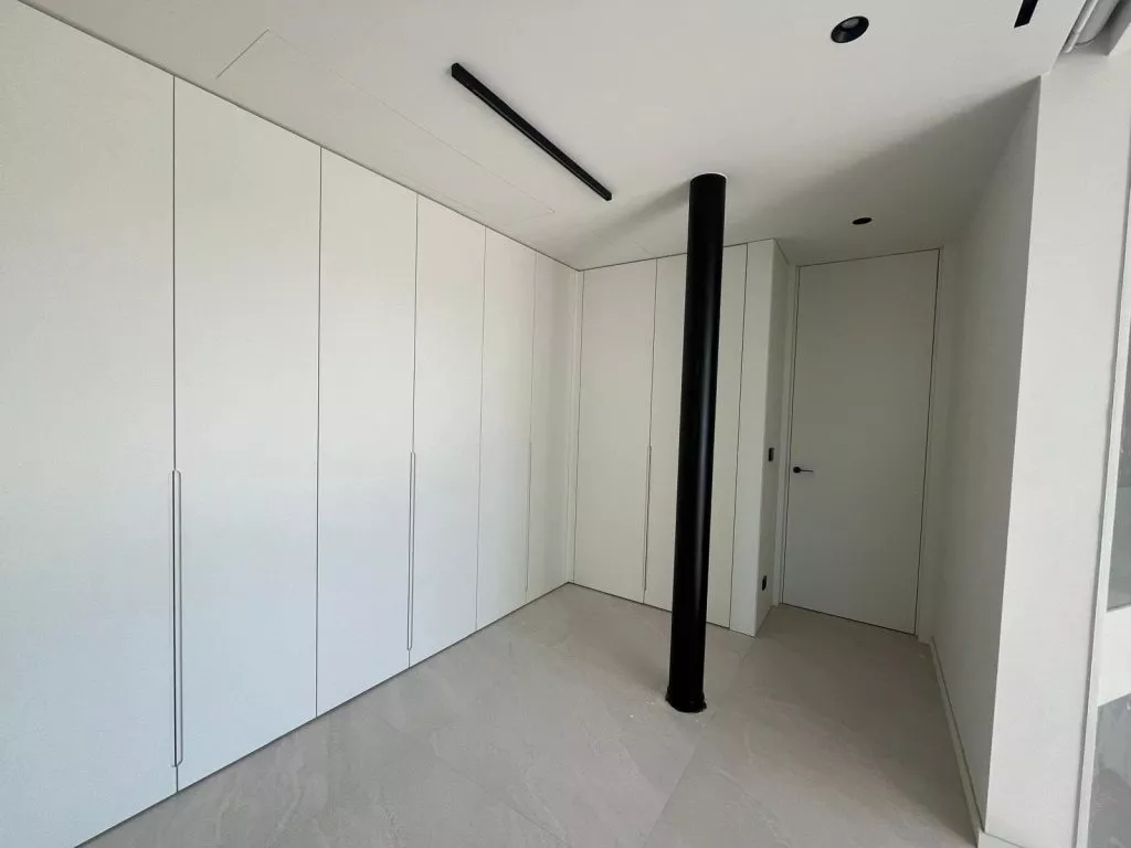 Armariets blancs minimalistes en un rebedor modern amb una columna negra i un terra de rajoles de color clar
