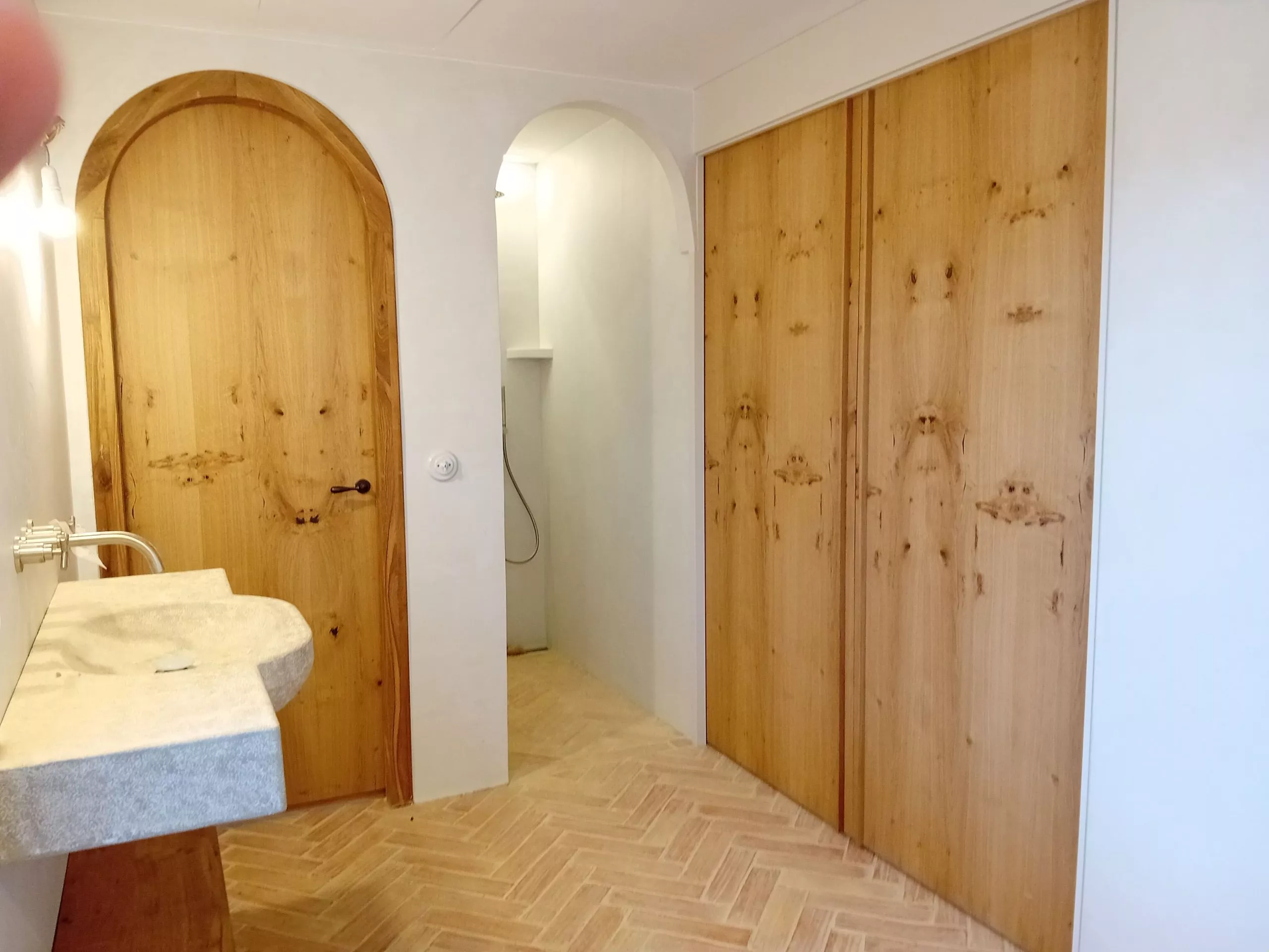 Baño con lavabo de piedra, puerta de madera arqueada y armarios de madera, mostrando carpintería a medida en proyectos