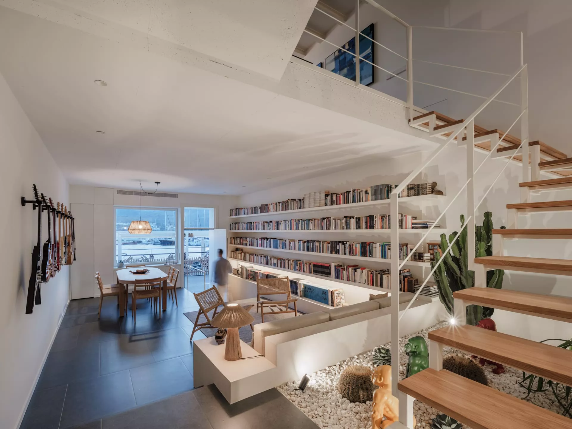 Salón moderno con estantería de libros a medida, comedor y escalera de madera, reflejando carpintería personalizada
