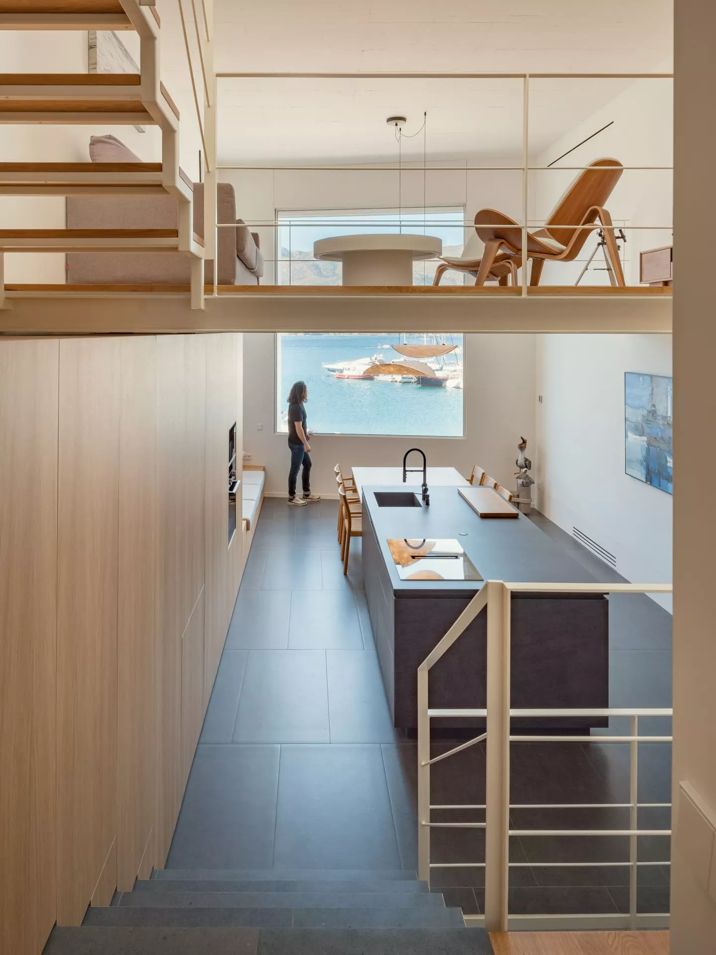 Diseño interior de CASA PDS con cocina moderna, escaleras de metal y madera, y vistas al mar con barcos.