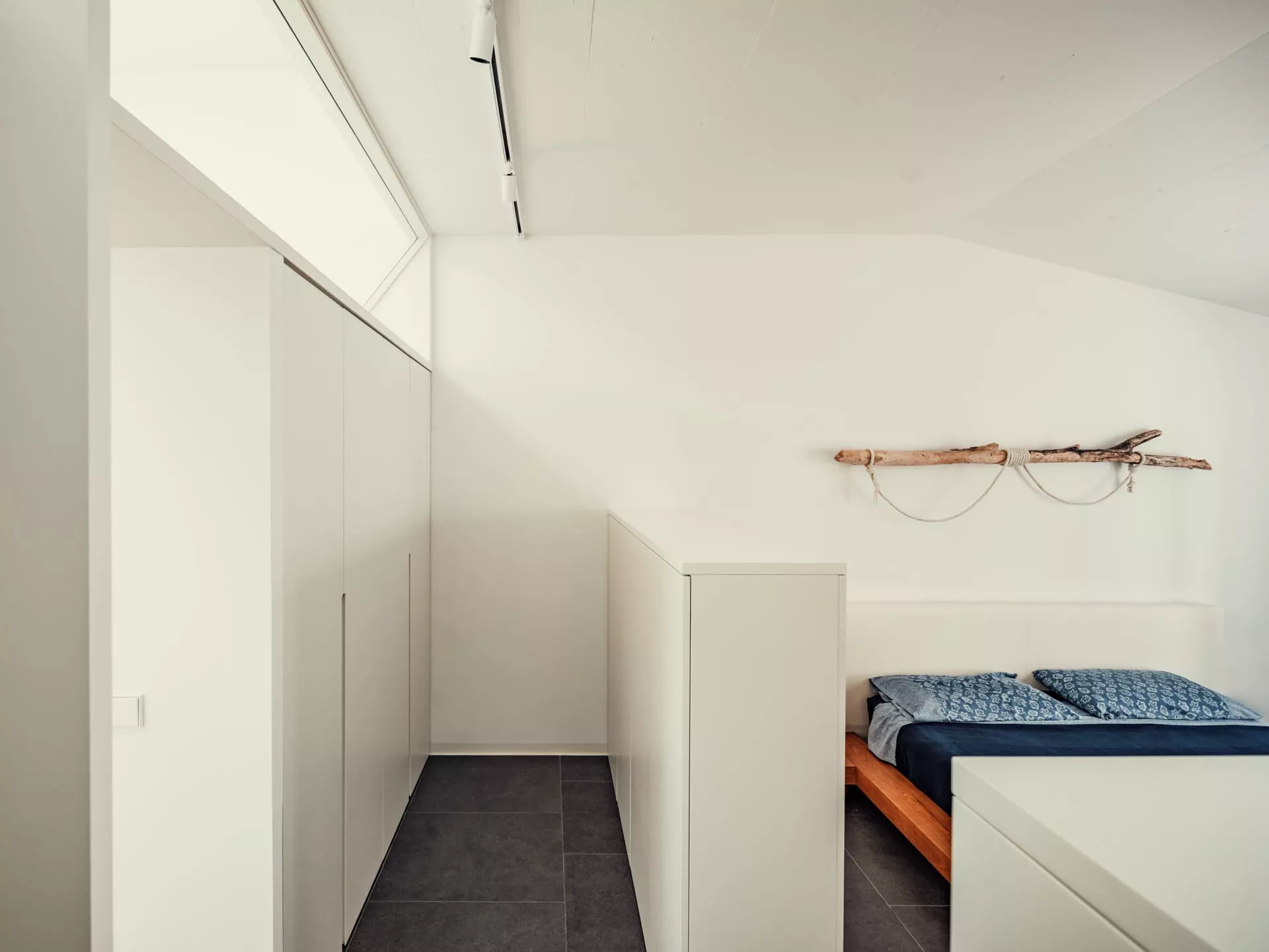 Dormitorio minimalista con cama de madera, ropa de cama azul, armario blanco y decoración de madera flotante en pared