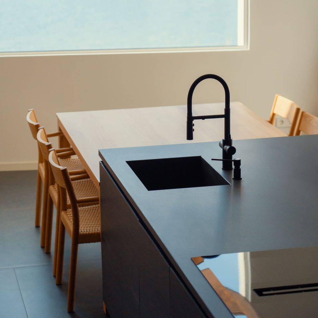 Cocina moderna con isla de carpintería a medida, fregadero negro y grifo minimalista, mesa de madera y sillas de diseño.