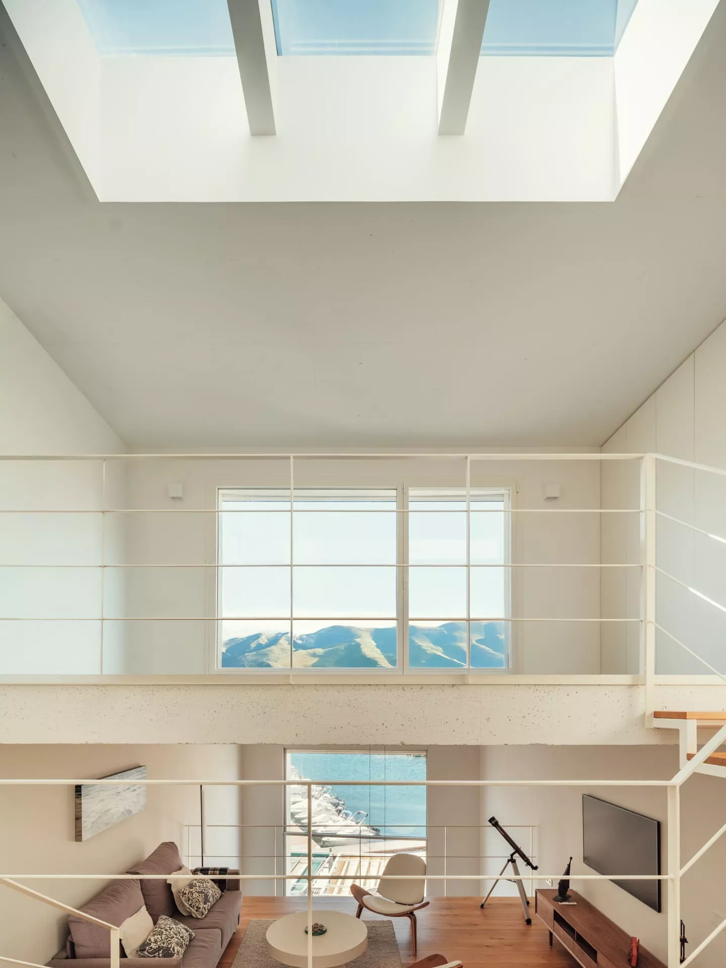 Interior moderno de vivienda con carpintería a medida, barandillas blancas y vistas al mar y montaña, diseño integral