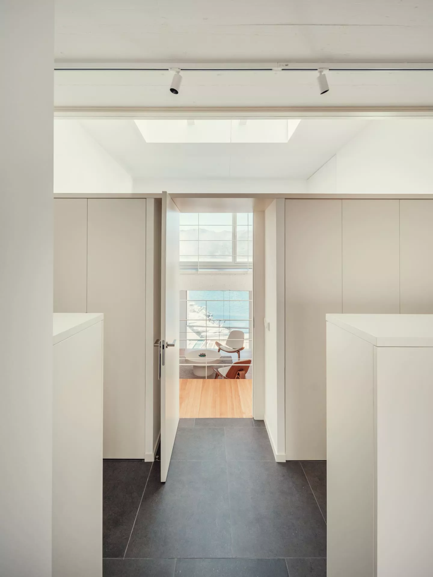 Pasillo moderno con suelo de baldosas oscuras y puerta abierta a sala de estar con vistas al mar, diseño de Fusteria Cano