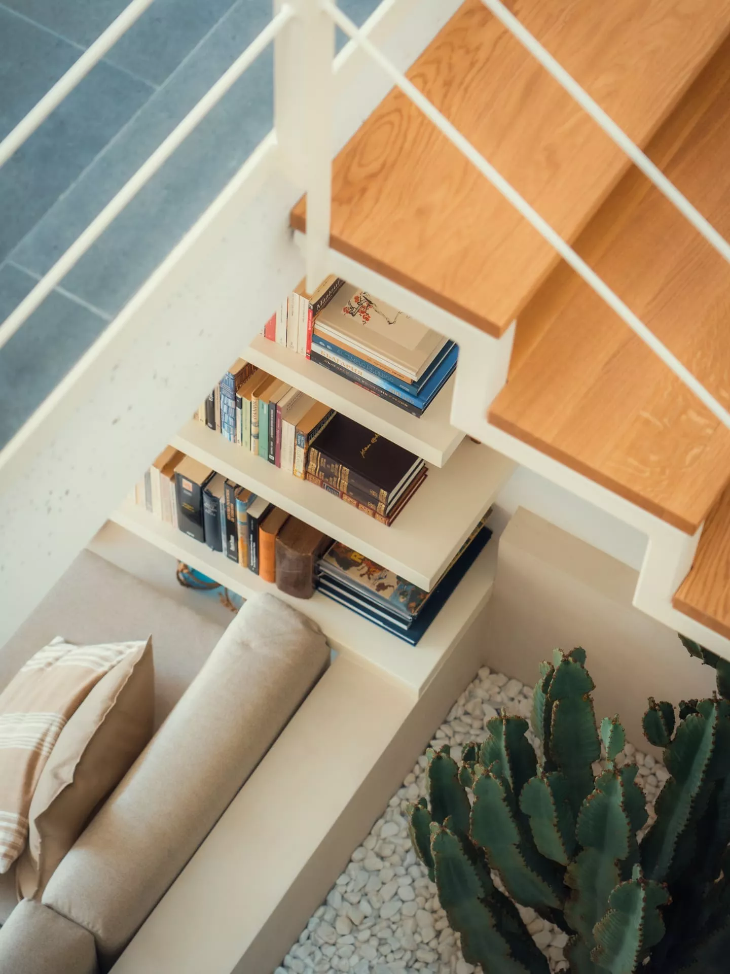 Estantería de madera a medida integrada bajo escalera, con libros y cactus, diseño interior moderno de carpintería