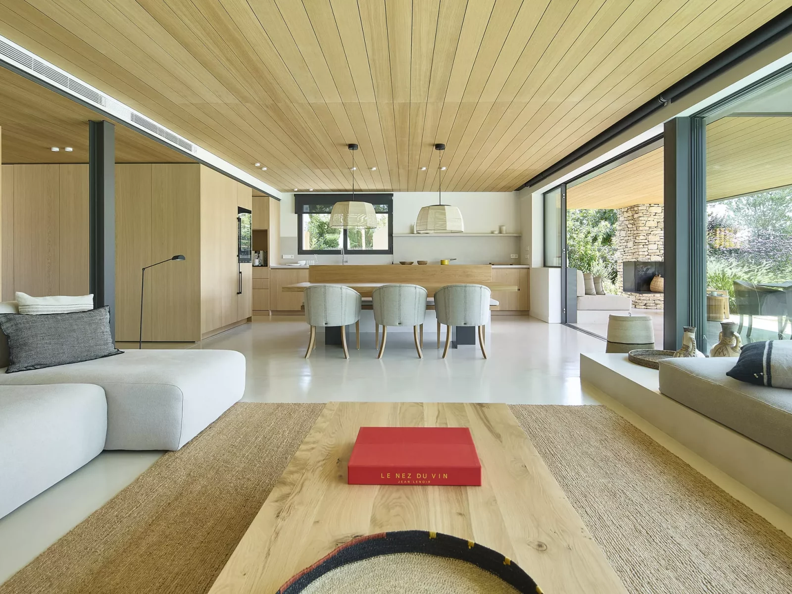 Salón y comedor de diseño moderno en CASA AAE con techo de madera, sofá claro, mesa de centro y acceso a jardín.