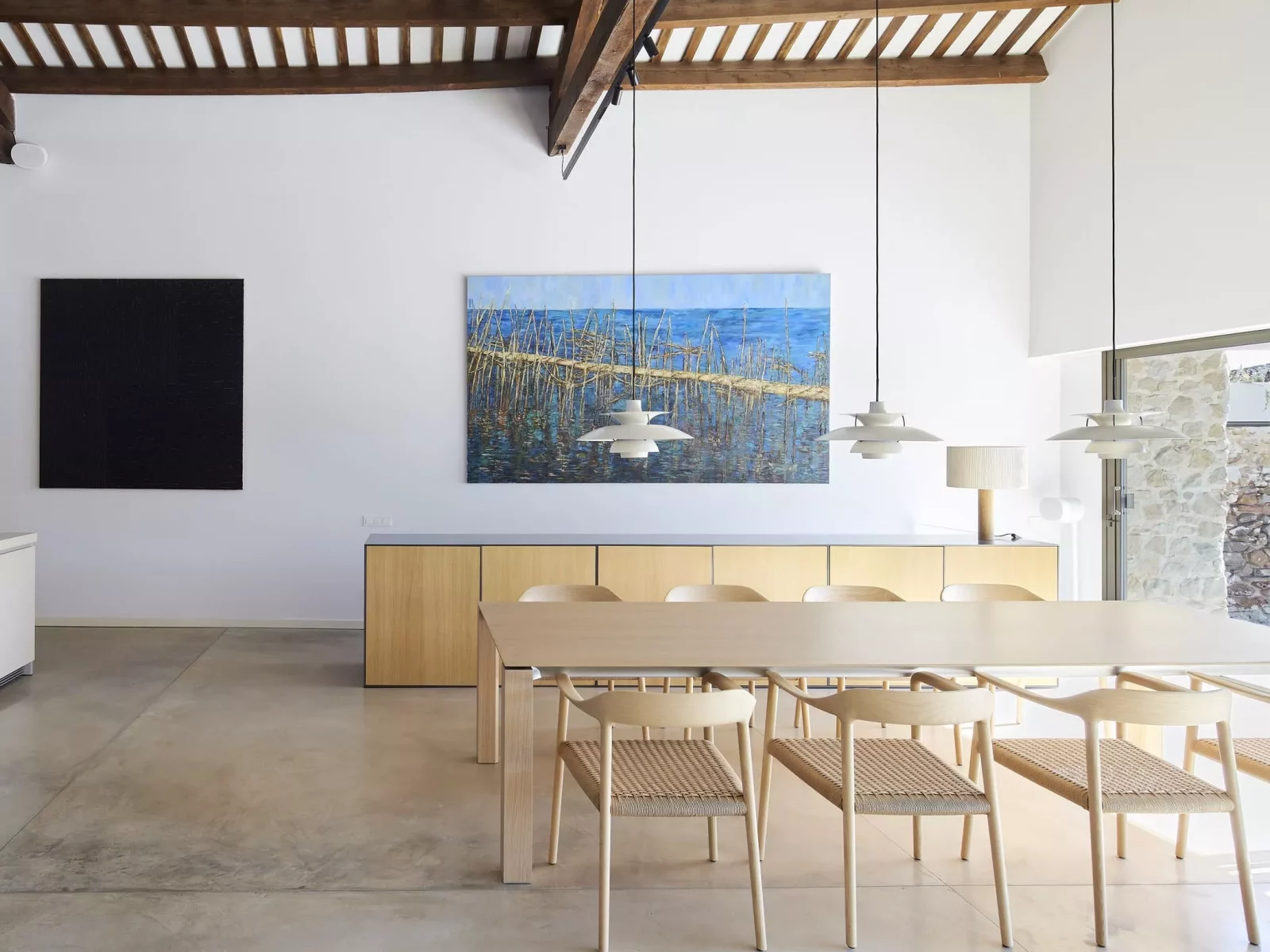 Comedor moderno con mesa de madera clara, sillas de diseño y arte abstracto en paredes blancas, destacando la fusteria a mida